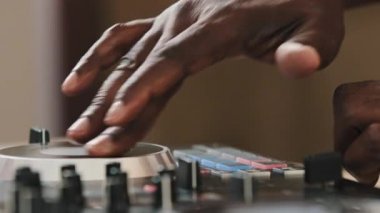 Close-up unrecognizable DJ man spinning record vinyl twist disc using mixer controller desk for playing electronic modern music in club party African male hands touching sliders sound audio recording