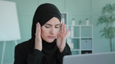 Tired Arabian Muslim Islamic woman in black hijab female worker student take short pause in online work feeling headache suffer with pain ache migraine employee overworked with laptop feel fatigue