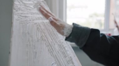 Close-up female dirty hand in white paint smears sticky plaster with palm fingers on canvas creates art emotionally painting unrecognizable artist woman doing masterpiece visual picture decorating