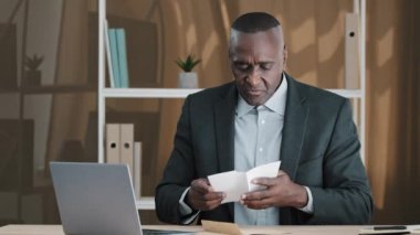 African old man senior mature male in office opening paper envelope reading letter with good news. Happy elder retired businessman received investment notification banking loan approval salary bonus