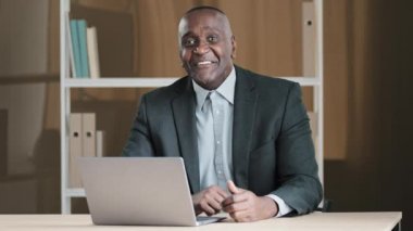 Old African 60s happy businessman laughing smiling sitting at office with laptop make you are right sign agree support good idea gesture approve nod head yes talking at camera video call conference