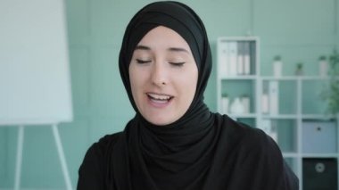 Webcam view happy smiling talking Muslim online teacher remote conversation Islamic woman in black hijab blogger vlogger influencer talking friendly at camera has video conference call online lesson