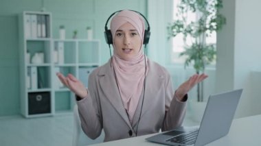 Muslim Islamic girl wearing hijab chatting with microphone and headphones working in call center talking using computer laptop presentation remote job meeting online class lesson webinar in headset