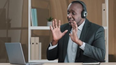 Old African American businessman online teacher professor leader remote consultant financial agent in headset talking video call consultation client show ten four fingers discussion advice negotiation