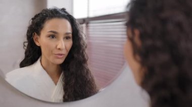 Young happy confident woman standing in bathroom looking in mirror rehearsing speech instructs preparing for interview says inspiring words motivates to win winks at reflection morning routine concept