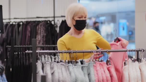 Mature Woman Customer Protective Mask Chooses Colorful Trendy Sweater Clothing — Stockvideo