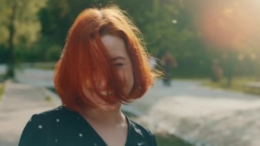 Portrait happy pretty caucasian red-haired beautiful attractive young girl student woman with short fluttering hair active moving flirting having good mood resting outdoors in park rejoicing weekend