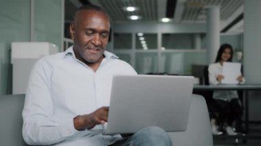 Elderly african businessman boss sit at coworking space modern office with laptop use computer technology wifi adult 50s american retiree entrepreneur working online in net typing email e-commerce job