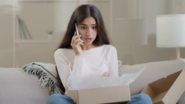 Angry dissatisfied client arabic middle eastern ethnic woman receive broken carton bad parcel delivery box having negative shopping experience telling complaints in mobile phone call negative feedback