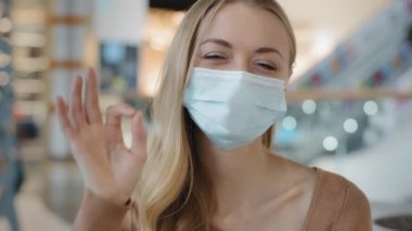 Portrait of young girl in protective medical mask caucasian woman showing sign okay joyful blonde looking at camera doing approve symbol gesture everything fine protection epidemic coronavirus concept