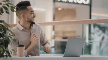 Cheerful hispanic man celebrating victory actively dancing arab guy sitting looking at laptop screen reading email with good news rejoices in success dance of winner win online lottery successful deal