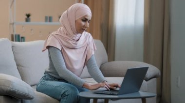Young muslim woman in pink hijab sitting on sofa working using laptop having headache migraine sad female freelancer feel severe pain tired stressed high pressure overtime work health troubles concept