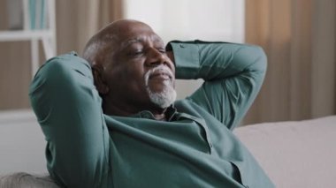 Portrait of contented elderly african american man smiling happy carefree grandpa resting at home holding hands behind head healthy calm retiree relaxing napping with eyes closed on comfortable sofa