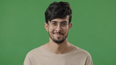 Portrait arabic young guy in studio on green background feel energetic close-up smiling bearded man with glasses looking at camera happy client satisfied with service in dental or ophthalmology clinic