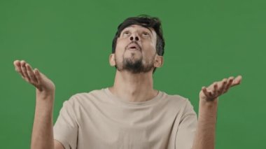 Portrait excited young hopeful arab man says prayer standing studio green background, hispanic praying asking for sign hope faith indian guy waiting God Allah ask good luck blessing raising hands up
