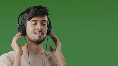 Close-up happy cheerful arabic man listen music use headphone enjoying song audio favourite pleasant tune carefree young hispanic guy satisfied high sound quality dancing to rhythm on green background