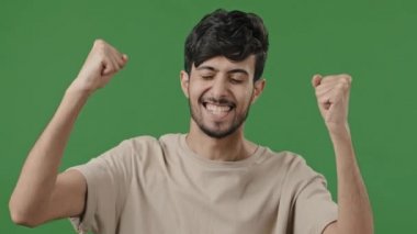 Joyful arabic guy in studio on green background celebrating victory happy young man looking at camera happy with good news winning gesture hispanic male feeling delight moment of win triumph concept