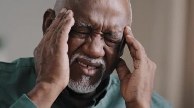 Close-up face sad elderly african american man feeling headache chronic migraine unhealthy multiracial grandpa massaging temples unhealthy middle aged 60s retired male suffering high blood pressure