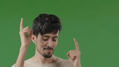 Close up smiling carefree arab guy dancing celebrating victory enjoy favorite music happy hispanic man moving rhythmically rejoice in success in studio on green background making movement with hands