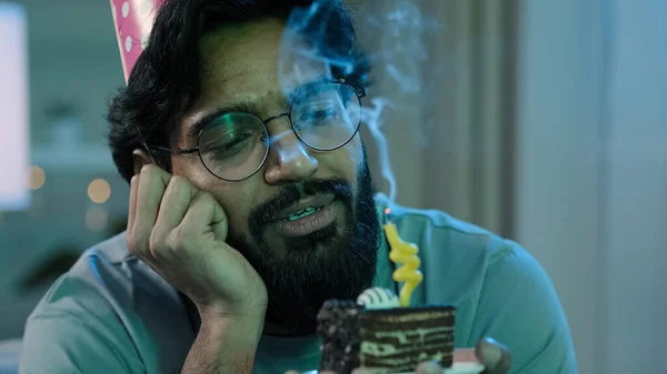 Headshot arabian alone single sad upset lonely bearded man in birthday pink hat and glasses sitting at home at night feel frustrated despair disappointed sadness holds cake with candle. High quality