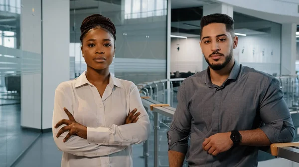 Business people African lady businesswoman and adult Arabian man boss manager standing in office and posing for camera with crossed arms. Two successful company workers in corporate workspace. High