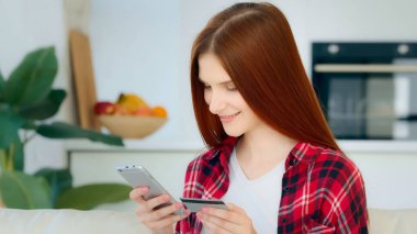 Satisfied caucasian female shopper customer enters number of bank credit card for financial transaction in mobile phone app makes donate pays internet order shopping online purchases booking e-tickets