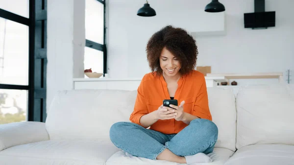 African American woman sitting home couch looking smartphone using phone play mobile game win victory reaction receive good offer opportunity news winning money prize make achieve triumph yes gesture