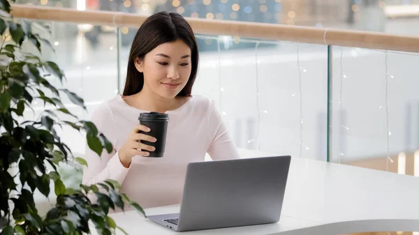 アジアの女子学生遠くノートパソコンビジネスカフェでオンライン教育を学ぶ女性フリーランスジャーナリストプログラマーカフェテリアに座ってコーヒーを飲む紅茶タイプのノートパソコン作業プロジェクトリモート — ストック写真