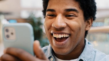 Close up African guy surprised by message received wins online bets looking at mobile phone opens mouth in surprise delighted shock man feels happiness from unexpected news amazing offer opportunity