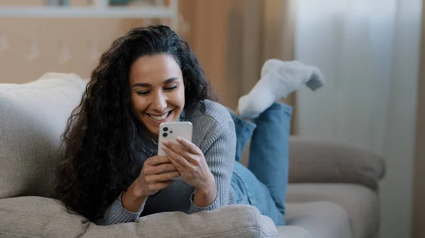 Happy Hispanic Young Woman Lying Sofa Typing Message Phone Smiling — Stok fotoğraf