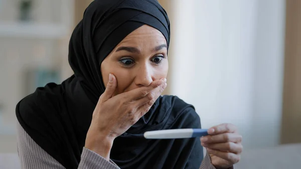 Joyful islamic young woman in hijab smiling happily holding pregnancy test excited pregnant lady surprised and happy celebrating good news future mother shows positive result muslim female expect baby