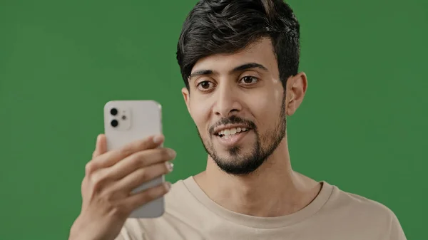 アラビア語若いです笑顔男作るビデオ通話の緑の背景でスタジオ使用して会議アプリ上の電話で楽しく友人とオンラインシェア良いニュース励起男波手開始ストリームライブ — ストック写真