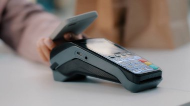 Resepsiyondaki kadın NFC aracılığı ile akıllı telefonla ödeme yapıyor. Bar kafedeki cep telefonundan yapılan ödemesiz yemek ürünleri satın alınıyor. Telefondan yakın çekimde terminale odaklanıyor.