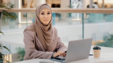 Odaklanmış ciddi Arap iş kadını profesyonel girişimci ofis masasında oturmuş dizüstü bilgisayara bakıyor online kurs müslüman kız serbest çalışan bilgisayar aygıtı kullanıyor.