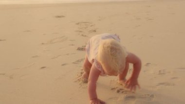 Cute funny small baby Caucasian baby little daughter newborn toddler infant crawling on all fours steps walking on sandy shore near ocean sea have fun playing outdoors in summer day child development
