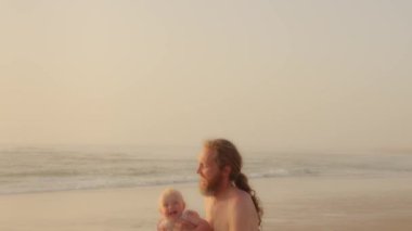 Happy family in seaside Caucasian bearded father playing with son daughter infant child near sea ocean water beach outdoors dad throw up in sky high rising kid newborn toddler and catches summer game