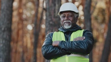 Olgun Afro-Amerikan özgüvenli erkek işadamı dışarıda duruyor profesyonel orman mühendisi ustabaşı üniformalı, koruyucu miğferli, kollarını kavuşturup kameraya bakıyor.