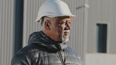 Portrait mature african american professional worker successful builder contractor foreman engineer architect wearing safety hardhat smiling looking at camera posing outdoors at construction site