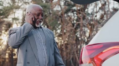 Mature african american businessman stands near car talking on phone confident man sales agent answering business call using smartphone customer confirming internet order in online store communicates