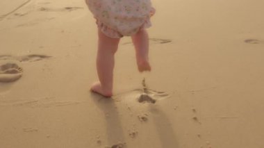 Closeup feet baby learns to walk on beachside on sand unknown barefoot kid toddler child unrecognizable daughter son make first steps learning walking on beach at summer going clumsily hot sandy coast