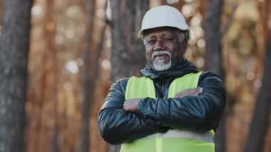 Mature developer forestry engineer foreman professional construction worker in uniform and protective helmet stands outdoors confidently posing with arms crossed smile approve shakes head in agreement