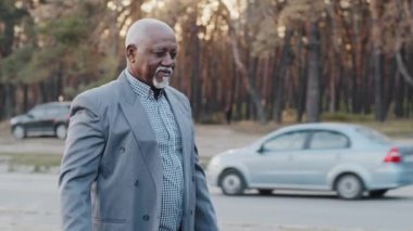 Mature african american businessman shopper walking down street coming back from store carrying gift bags with purchases puts packages in trunk of car elderly man happy with purchase at discount sale