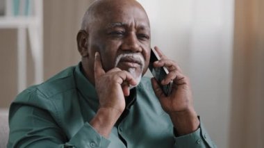 Old bald African businessman with gray beard aged male client thinks speaking on the phone remembers remote consultation loses forgets memory problems business troubles failure headache pain stress