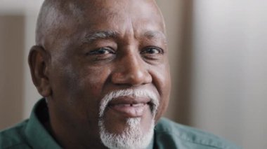 Portrait close clever serious pensive male wrinkled face with gray beard bald African old senior mature thoughtful businessman looking away thinking pondering turning head looks at camera smiling