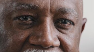 Macro extreme close up half part of face elderly middle-aged African old wrinkled man with dark eyes sad calm mature male senior citizen looking at camera myopia vision sight problem poor eyesight