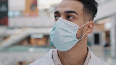Spanish Arabic Indian medic worker man doctor in respiratory mask uniform therapist surgeon dentist male nurse indoor in hospital looking away thinking turning to camera student of medical university