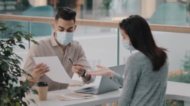 Arab Indian businessman salesman insurance agent realtor manager bank worker wears medical mask advises client woman consultation with papers sells auto real estate girl signs contract document offer