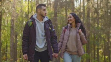 Couple in love enjoying walk in autumn forest holding hands talking young adventurous hikers walks in park traveling with backpack admire surroundings happy girlfriend pointing at beautiful landscape