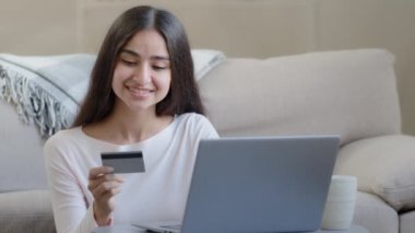 Happy female arabian consumer shopper hold plastic banking card enter numbers for online bank app pay money deposit use credit limit donate for charity transfer electronic savings for delivery service