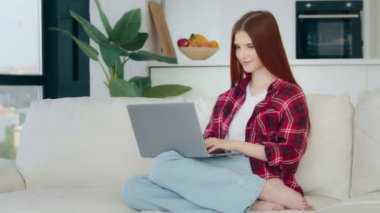 Successful young business woman freelancer student redhead girl works on laptop at home communicate in virtual chat use internet home wifi looking at camera makes okay good gesture approval agree sign